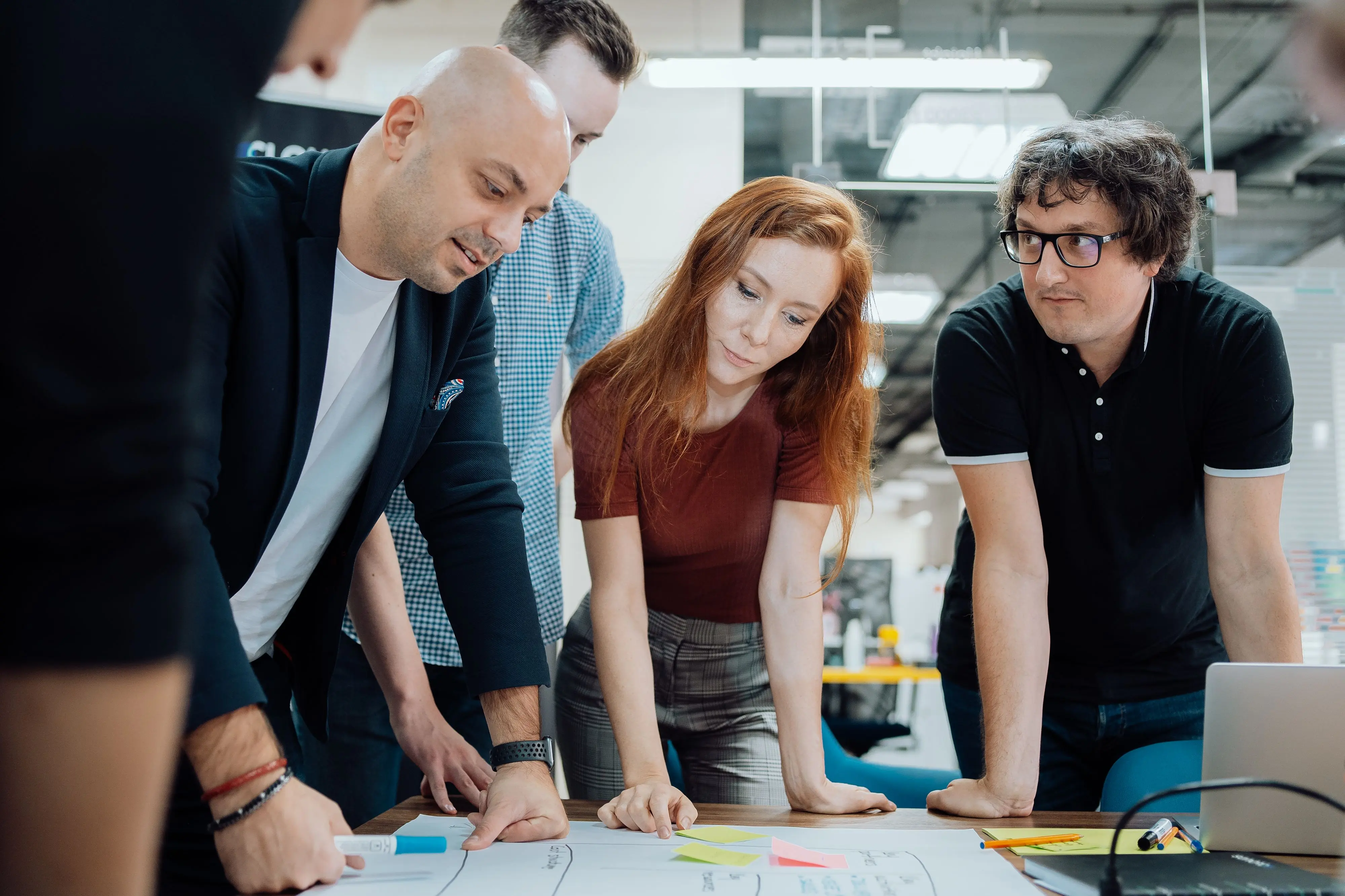 Five people in informal clothes gathered around a table in a boardroom discussing the contents of a product plan 